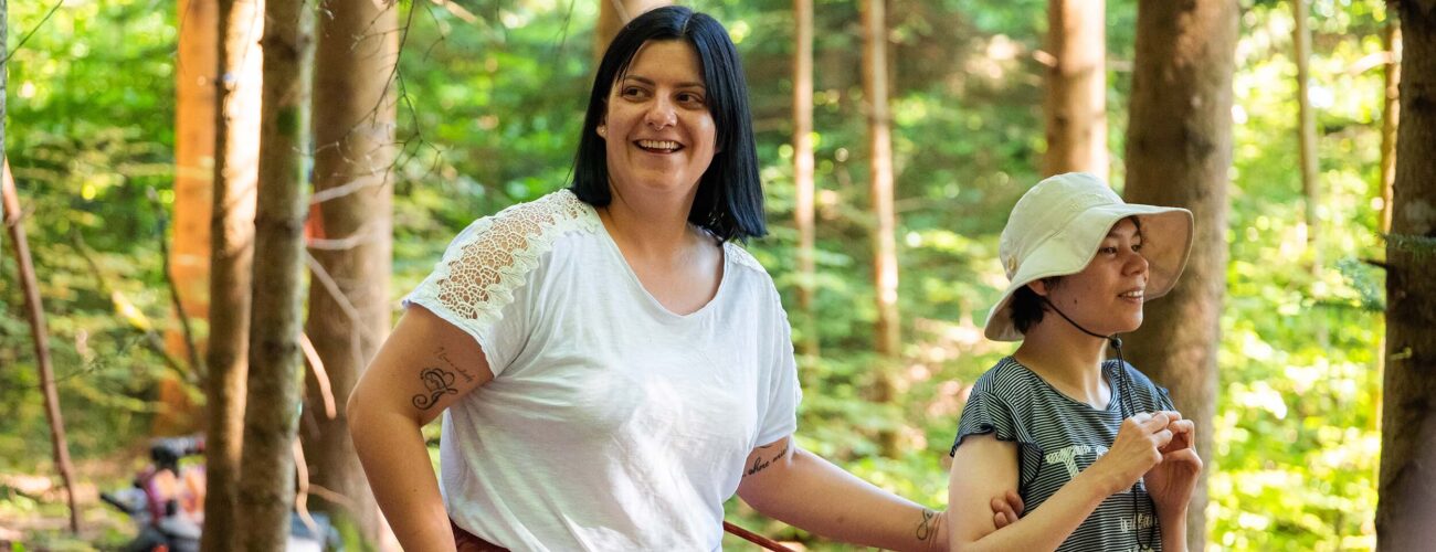 Eine Mitarbeiterin des Ateliers begleitet eine Klientin im Wald beim Spielen