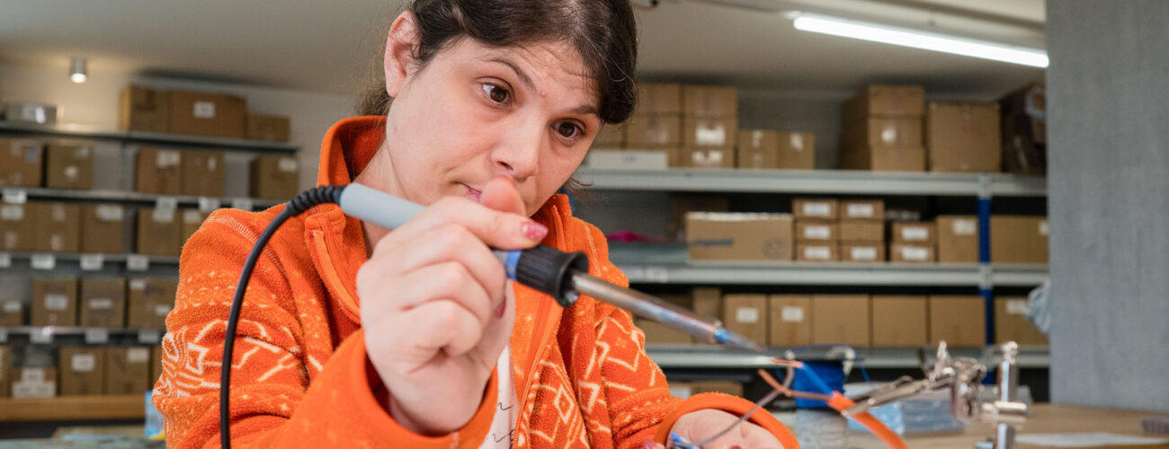Eine Mitarbeiterin lötet konzentriert ein Kabel