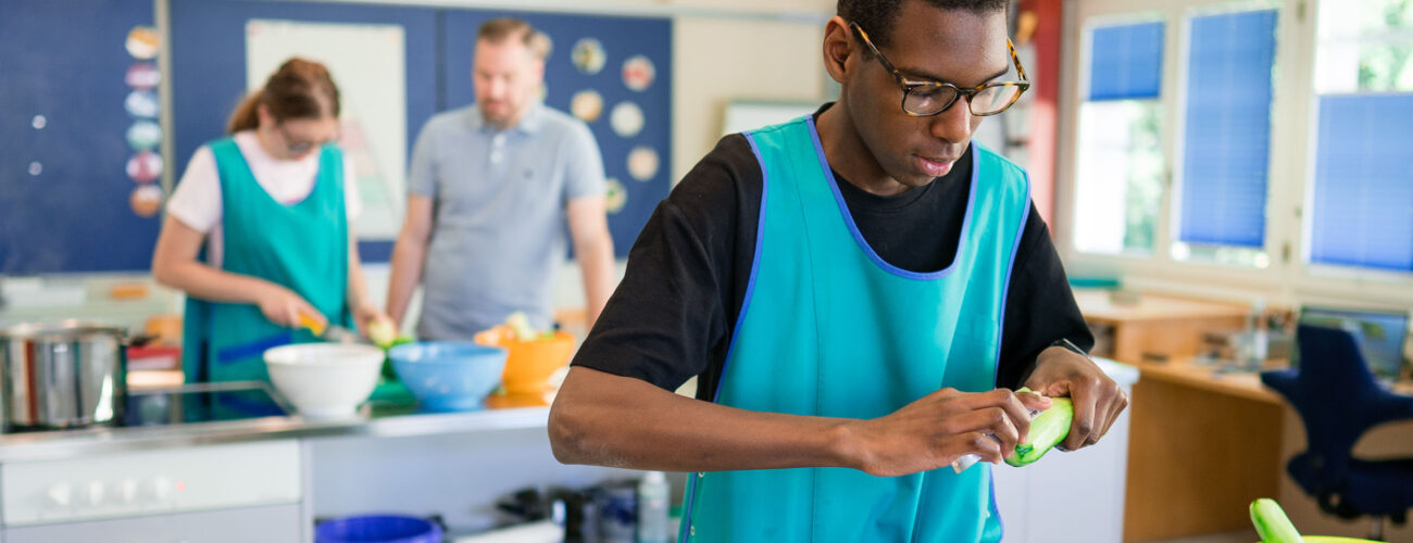 Ein Schüler rüstet in der Kochgruppe eine Gurke