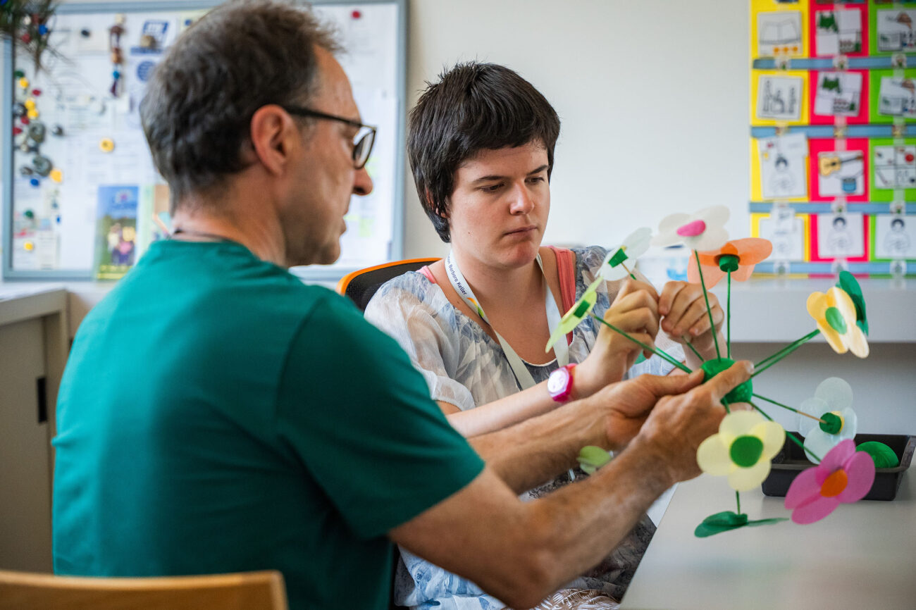 Ein Mitarbeiter des Ateliers hilft einer Klientin beim Basteln